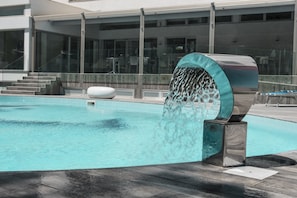 A modern pool with a water feature, surrounded by a glass railing and steps leading to a building with large windows. - Homeholiday Giulivo (Cellole)