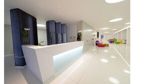 A modern reception area with a white reception desk, a blue accent wall, and colorful seating in the background. - Homeholiday Giulivo (Cellole)