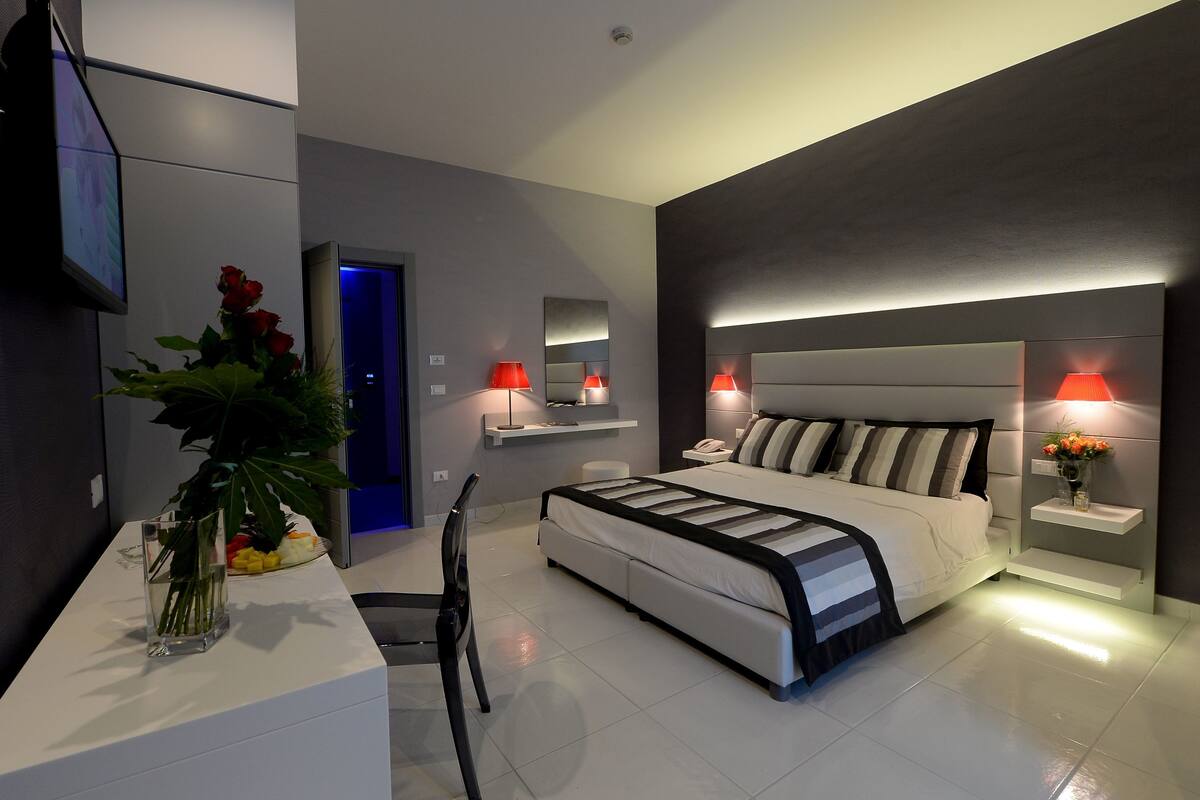 Ein modernes Schlafzimmer mit Bett, Nachttischen, einem Fernseher und einem Schreibtisch mit Blumen.