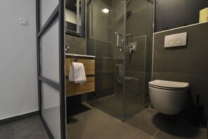 A modern bathroom with a glass shower enclosure, a toilet, and a wooden vanity with a towel hanging. - Mono Apartments & Rooms (Zadar)