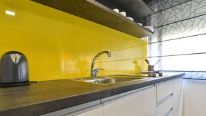 A modern kitchen with a yellow backsplash, stainless steel sink, and white cabinets. - Mono Apartments & Rooms (Zadar)