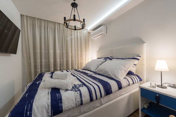 Een net opgemaakt bed met gestreepte beddengoed, een bedlampje en een klein nachtkastje met een lamp.