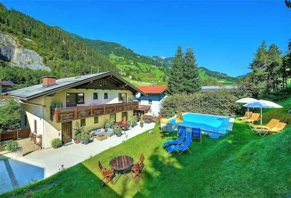 A chalet with a swimming pool, outdoor seating, and a mountain backdrop.
