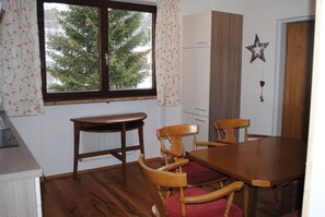 A dining area with a wooden table and chairs, a radiator, and a window with curtains.