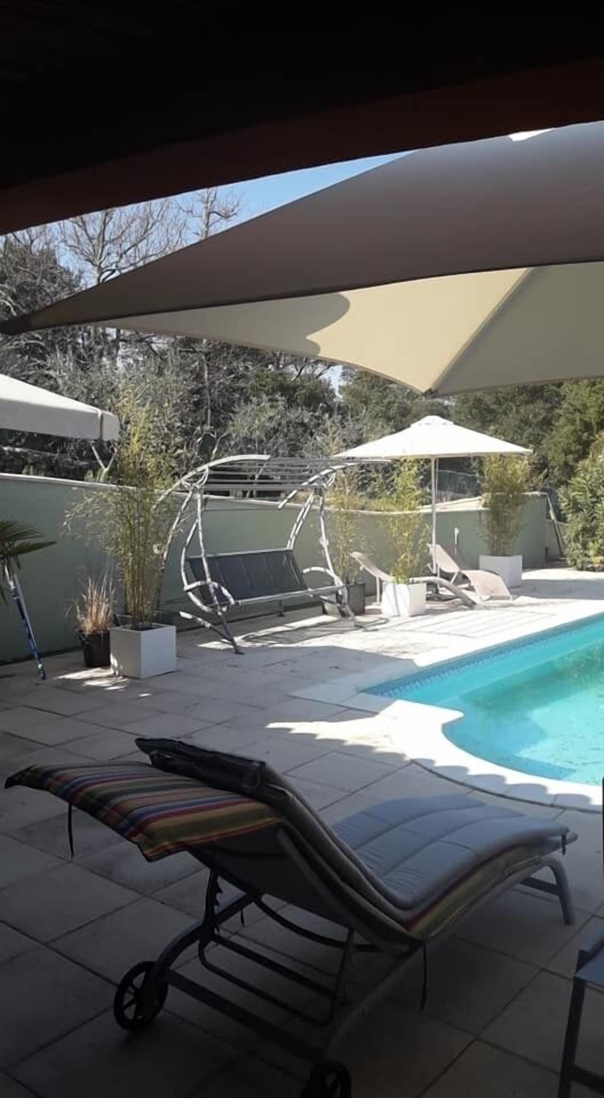 A poolside area with lounge chairs, a small table, and potted plants.