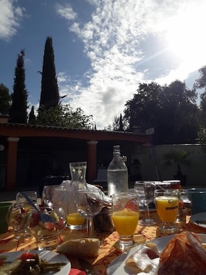 An outdoor dining table with various food items and drinks, set against a backdrop of trees and a clear sky. - Villa Catharina (Lorgues)
