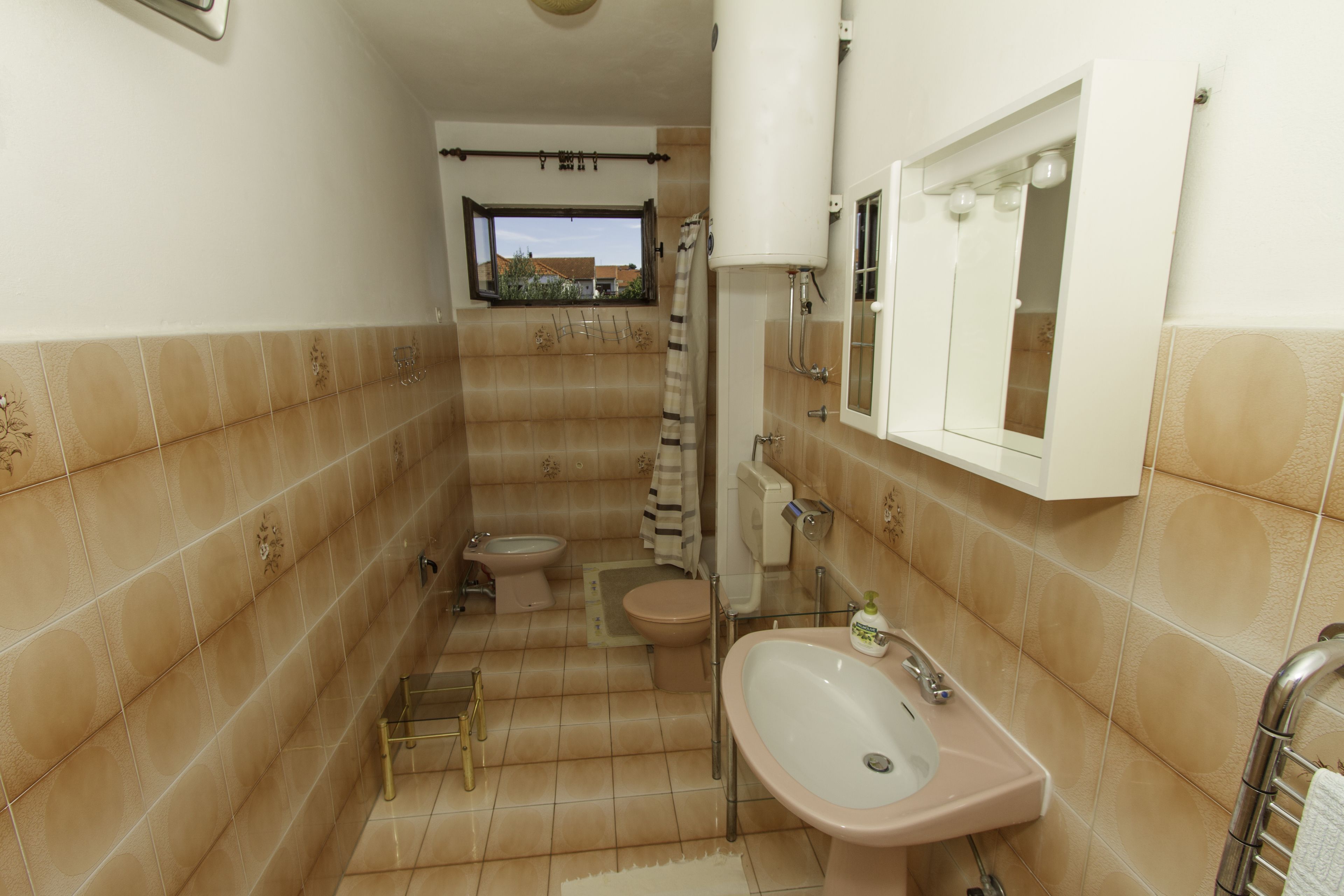Un baño con lavamanos, inodoro y bidé. Cuenta con un ventanal con vistas a edificios.