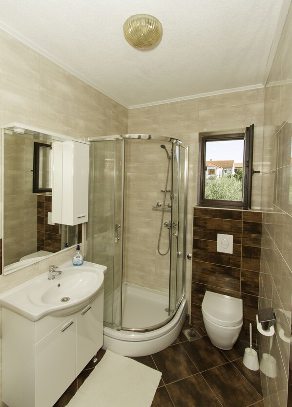 A modern bathroom with a glass-enclosed shower, a white sink, and a toilet. - Apartments Joso (Zadar)