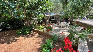 A garden with trees, a stone bench, and a table with chairs. - Apartments Joso (Zadar)
