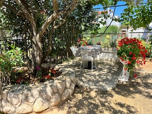 An outdoor patio with stone walls, a table with chairs, and red flowers. - Apartments Joso (Zadar)