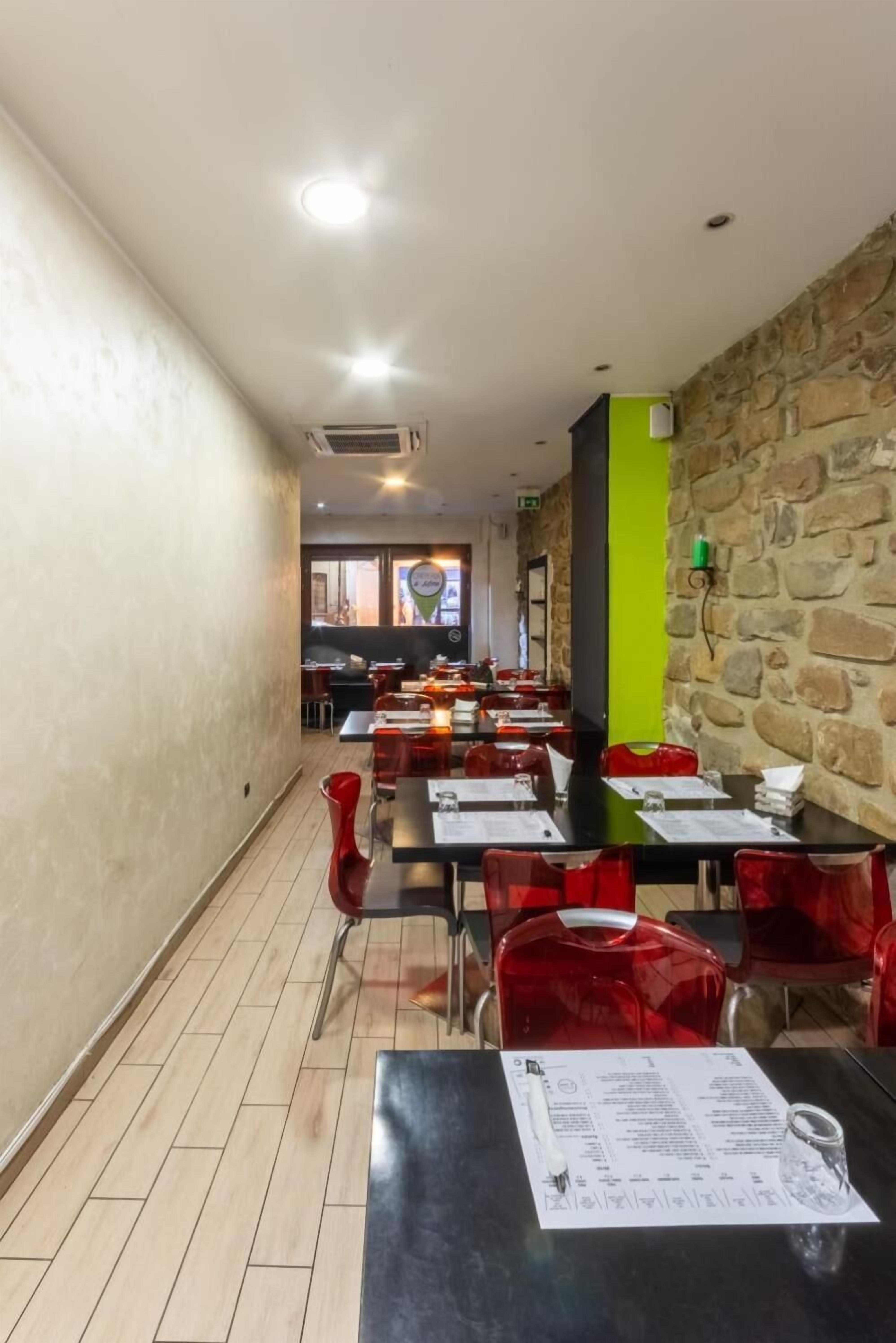 Un restaurant avec des tables et des chaises, un mur en pierre et un pilier vert.