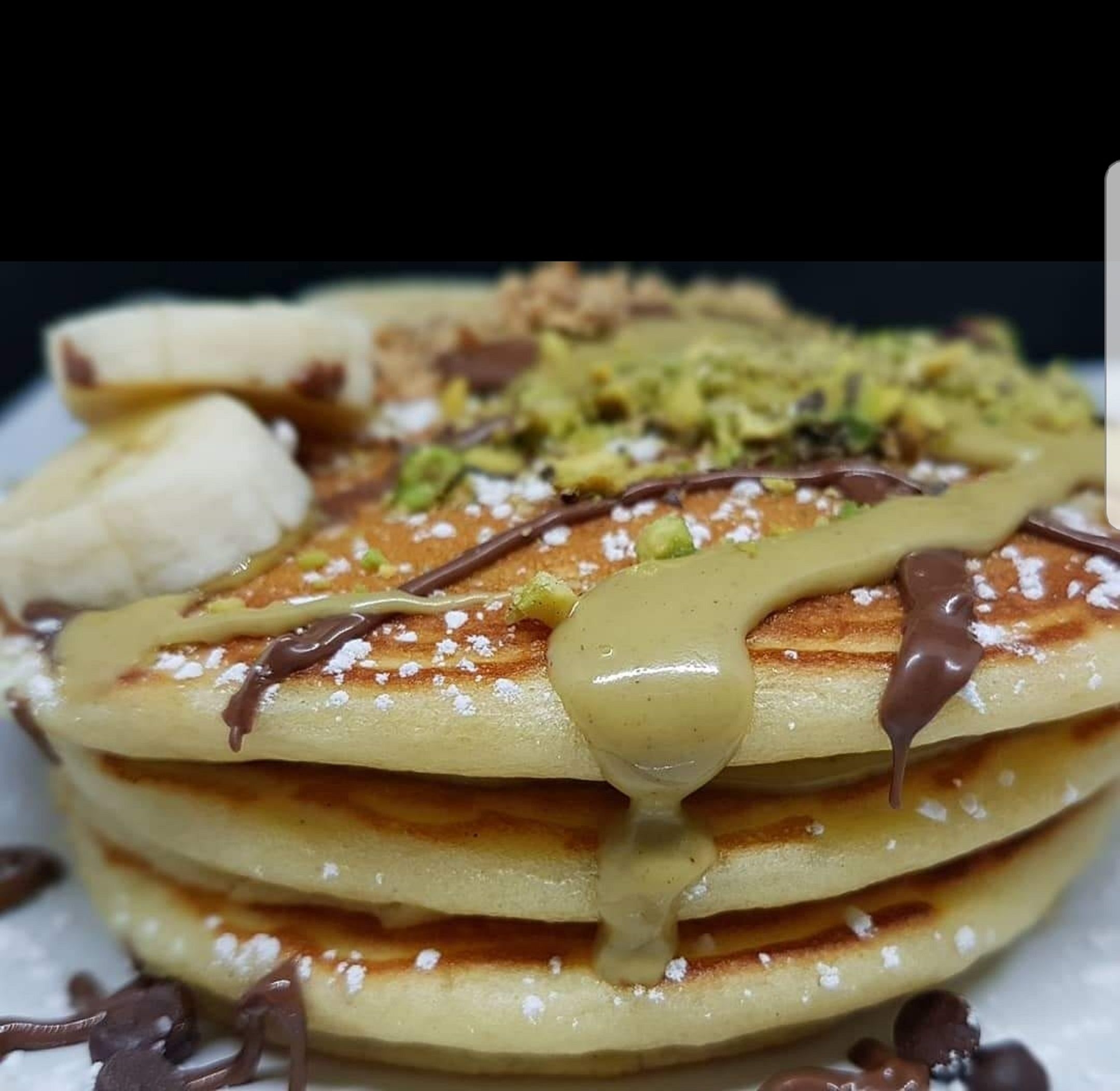 Une pile de crêpes nappées de sauce au chocolat et saupoudrées de sucre glace.
