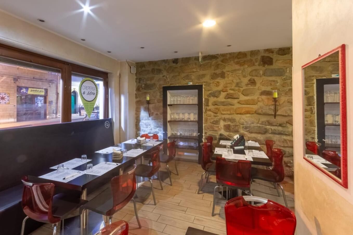 A restaurant with a stone wall interior, multiple tables with menus, and red chairs.