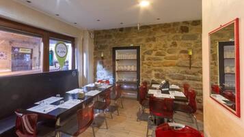 A restaurant with a stone wall interior, multiple tables with menus, and red chairs.