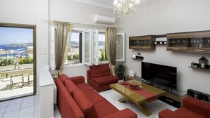 Uma sala de estar moderna com um amplo sofá, uma TV e uma varanda com vista para o mar.