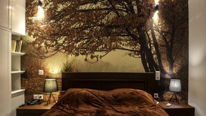 Quarto com uma cama grande, duas mesas de cabeceira com luminárias, uma estante e um mural de árvore na parede.