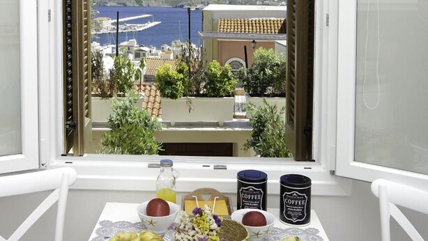Varanda com mesa posta para o pequeno-almoço, com vista para a costa, edifícios e um porto de recreio.