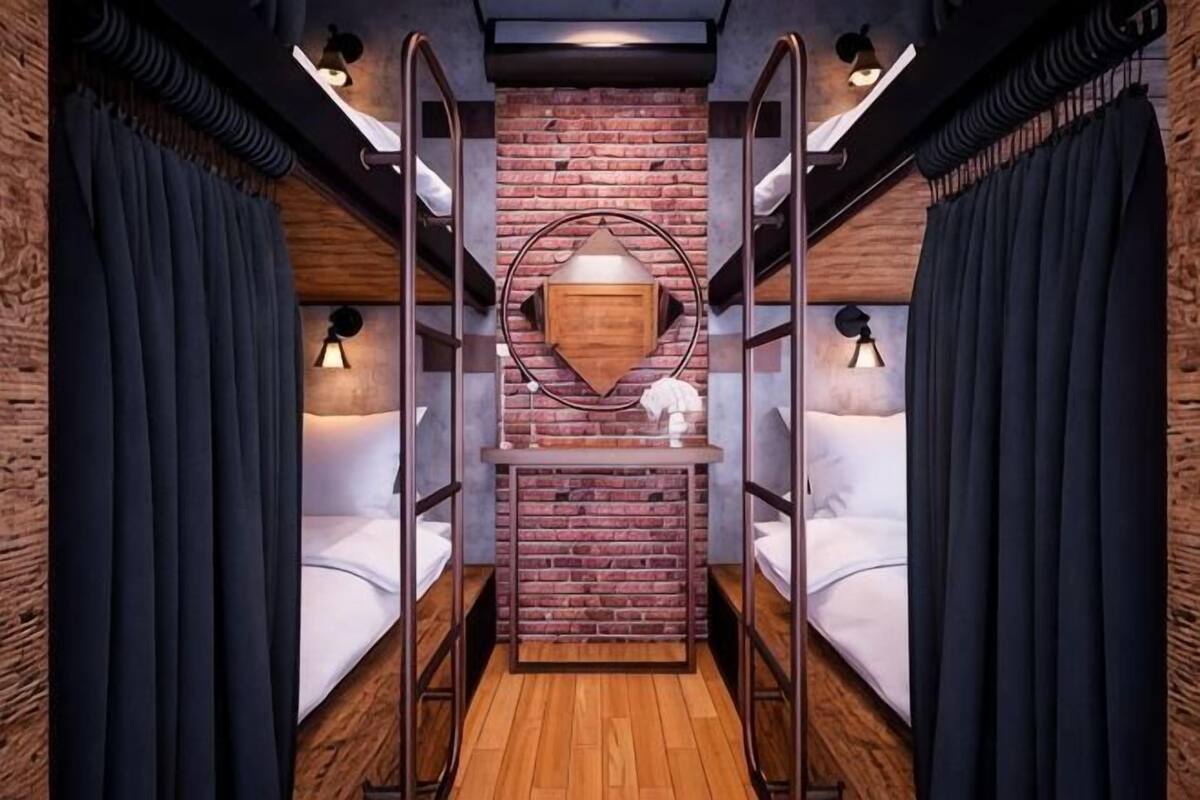 A narrow, enclosed room with bunk beds, a wooden floor, and a brick wall.
