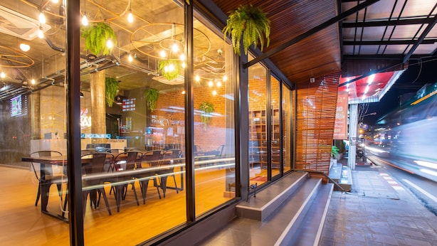 A modern restaurant with large windows, hanging plants, and a wooden interior. - Kaen Hostel (Pattaya)