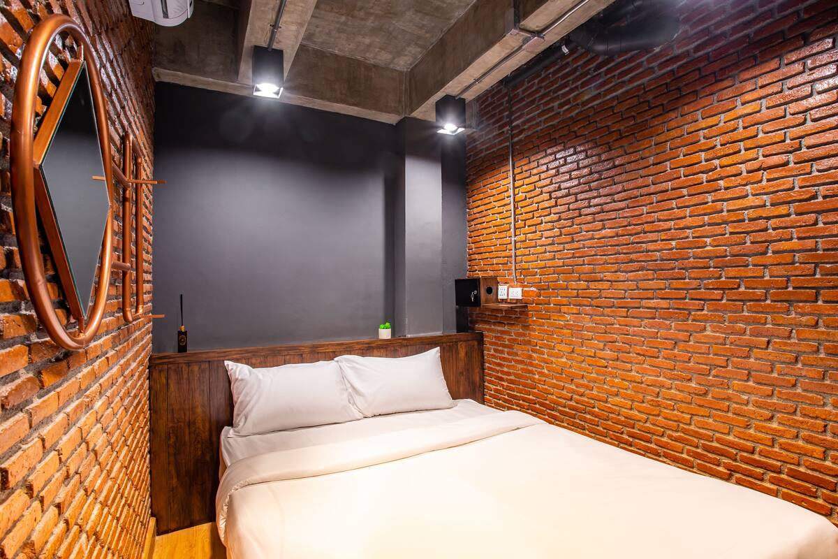 A neatly made bed with white linens, a wooden headboard, and a brick wall behind it.