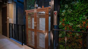 An elevator with a digital display, a metal door, and a green wall with plants. - Kaen Hostel (Pattaya)