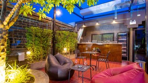 An outdoor seating area with a bar, cushioned seating, and a view of the sky. - Kaen Hostel (Pattaya)