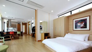 A modern hotel room with a large bed, a desk, and a kitchenette in the background. - Equinoxe de Geumneung (Jeju City)