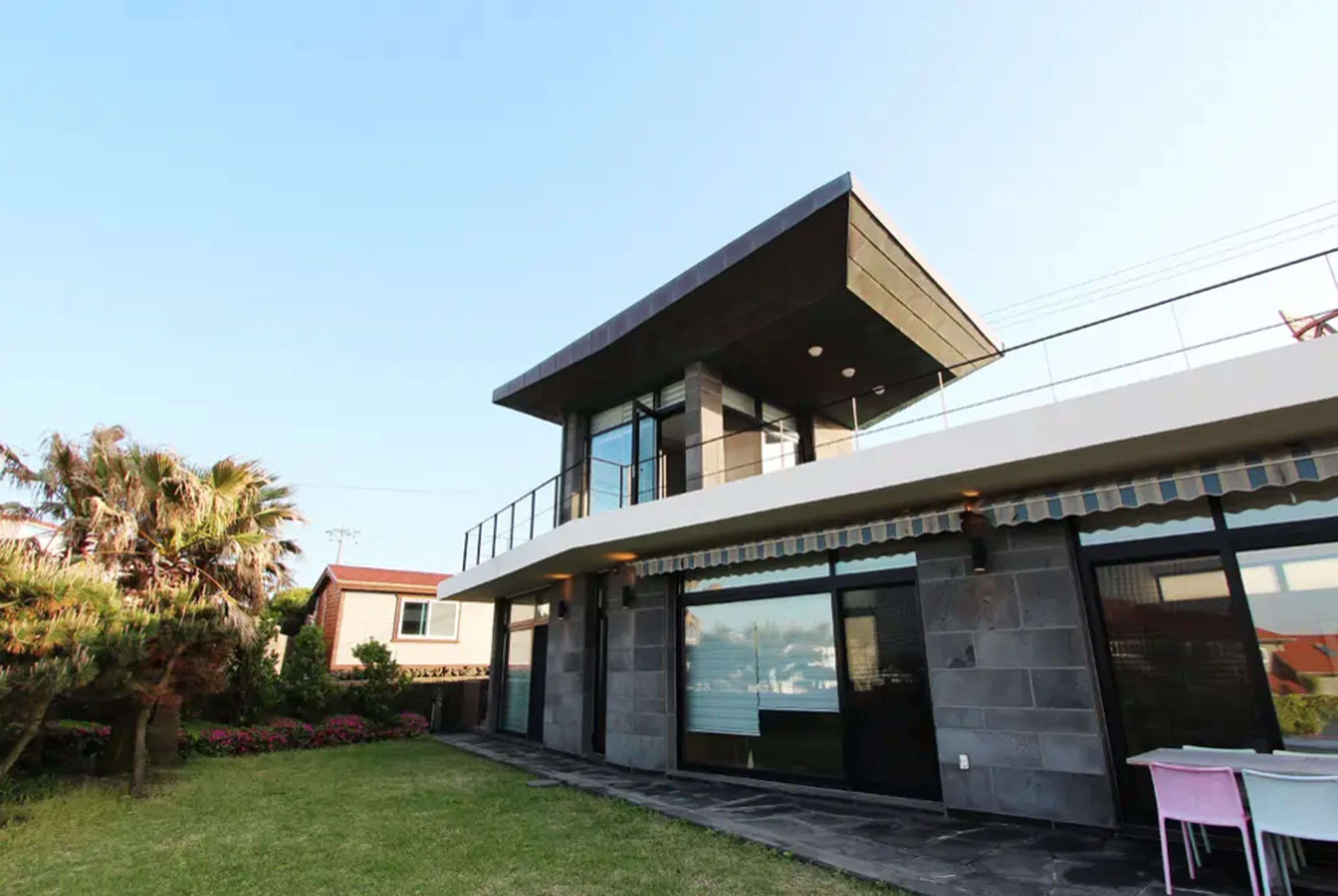 A modern two-story house with a flat roof, large windows, and a balcony.