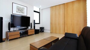 A modern living room with a flat-screen TV, wooden flooring, a black sofa, and a wooden wall panel. - Equinoxe de Geumneung (Jeju City)