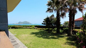 A grassy outdoor area with a stone pathway, palm trees, and a view of the sea. - Equinoxe de Geumneung (Jeju City)