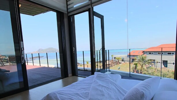 A bedroom with a large bed and a view of the beach and ocean through large glass doors. - Equinoxe de Geumneung (Jeju City)