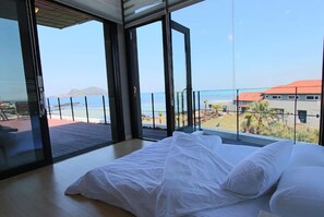 A bedroom with a large bed and a view of the beach and ocean through large glass doors. - Equinoxe de Geumneung (Jeju City)