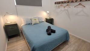 A bedroom with a bed, two bedside tables, a hanging light, and a wall-mounted coat rack. - Ohana Hawaiian term meaning "family" (Agnes Water)