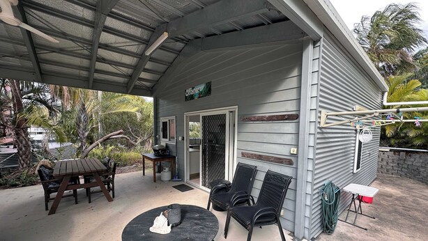 A covered outdoor area with a table and chairs, a small table with a chair, and a door leading to a screened porch. - Ohana Hawaiian term meaning "family" (Agnes Water)