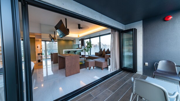 A modern living room with a sofa set, a dining area, and a kitchen visible through a glass door. - HOTEL Viviana (Naha)