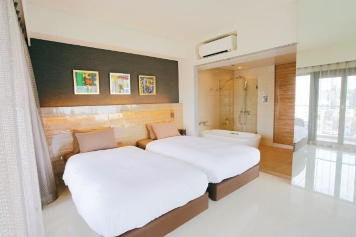 Una habitación de hotel con dos camas, zona de ducha y obras de arte en la pared.