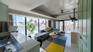A modern living room with a sofa, a small table, and a view of the city through large windows. - HOTEL Viviana (Naha)