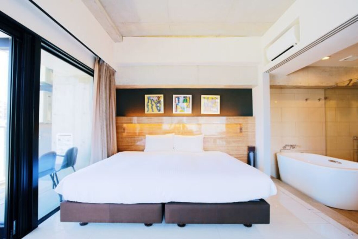 Una habitación de hotel moderna con una cama grande, una bañera y obras de arte en la pared.