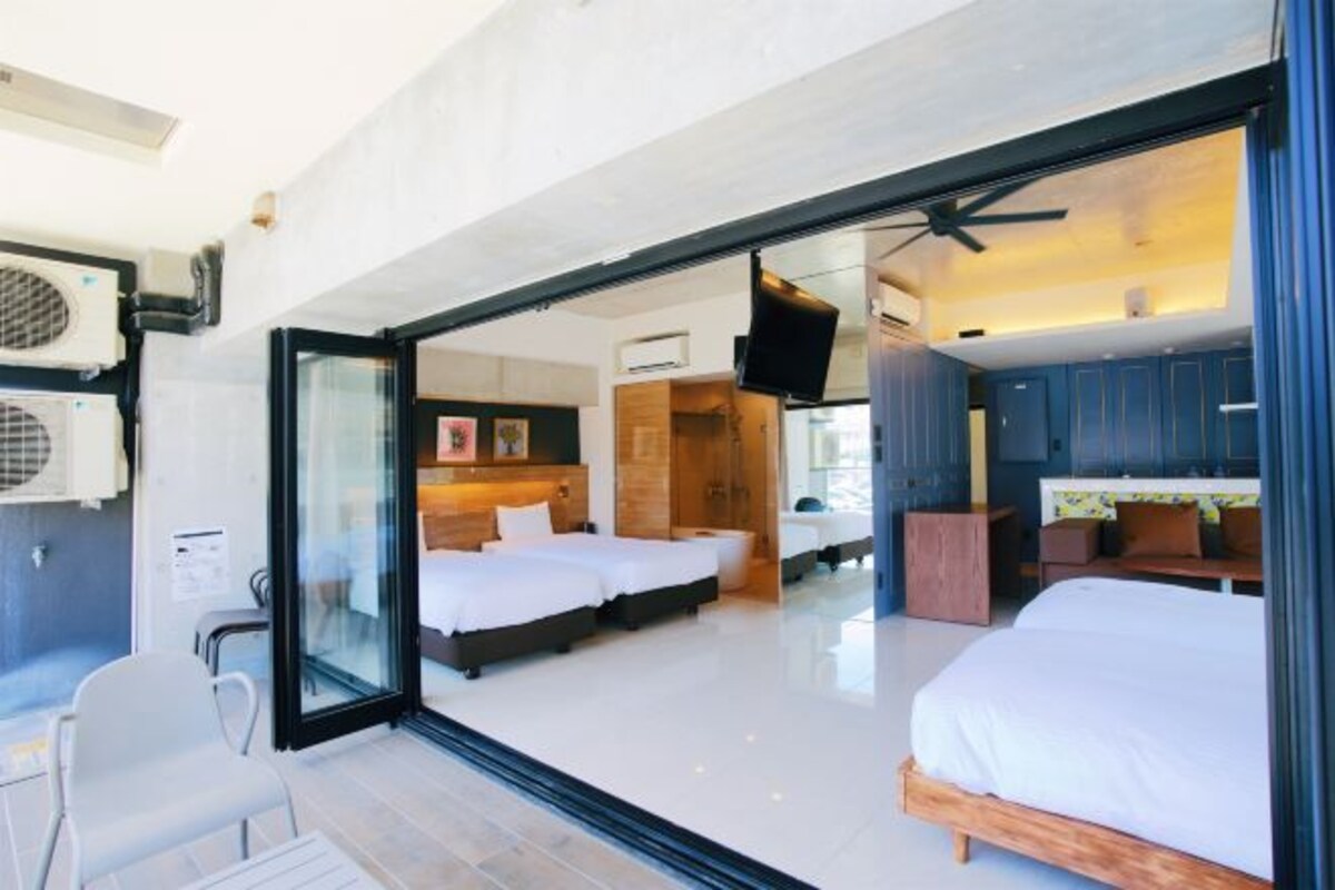 Habitación de hotel moderna con un amplio ventanal que da a un balcón, una cama, un escritorio y un televisor.