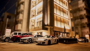 A parking lot with several luxury cars parked in front of a modern building with multiple floors and large windows. - HOTEL Viviana (Naha)