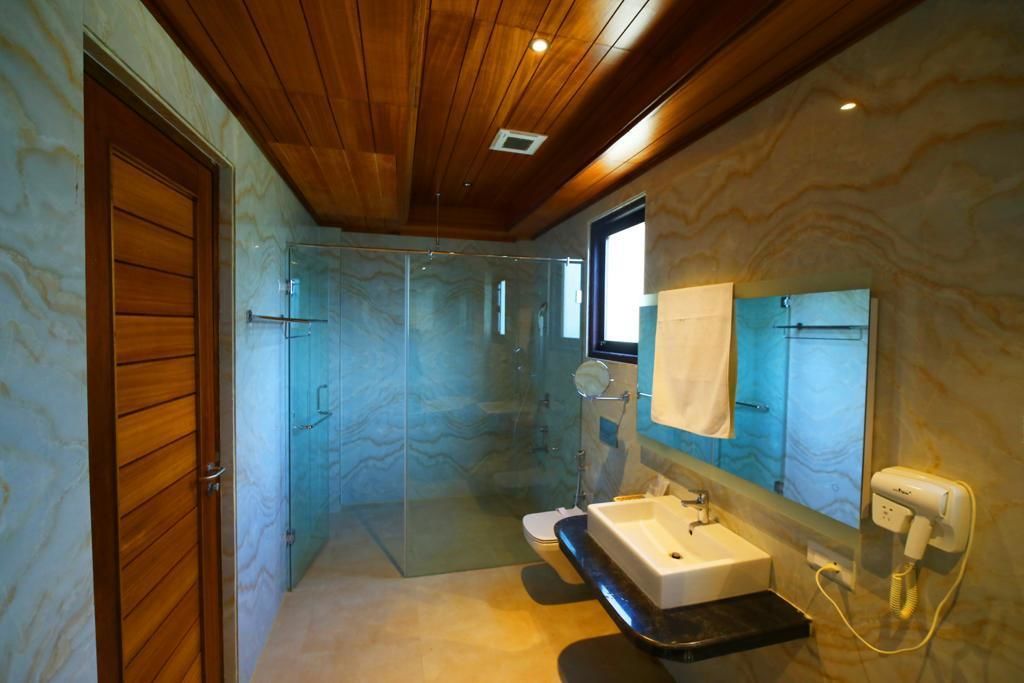 Ein modernes Badezimmer mit einer Duschkabine aus Glas, einer Holztür, einer Marmorwand, einem Waschbecken und einem Spiegel.