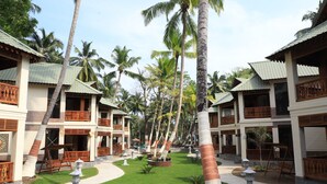 A resort with multiple two-story buildings, each featuring balconies with wooden railings, surrounded by palm trees and a well-maintained lawn. - Sandyy Wavess Beach Resort (Port Blair)