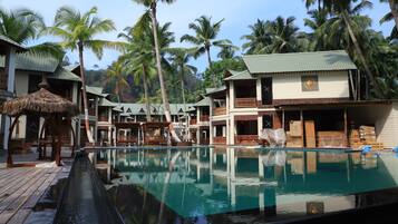 A resort with a swimming pool, wooden deck, and multiple bungalow-style buildings surrounded by palm trees.