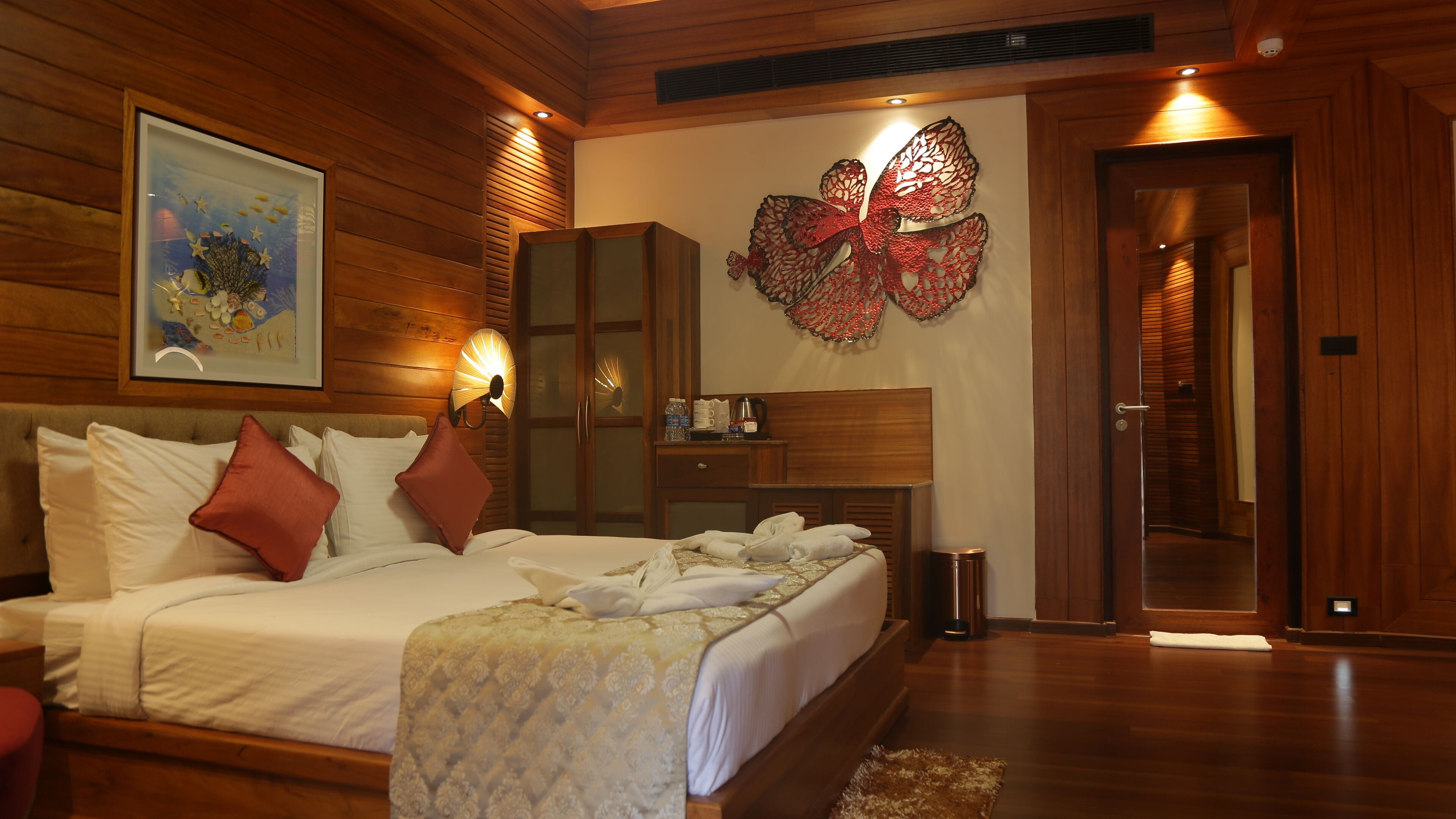 Une chambre d’hôtel avec un grand lit, une tête de lit en bois, une œuvre d’art accrochée au mur, un élément décoratif mural et une porte en bois.