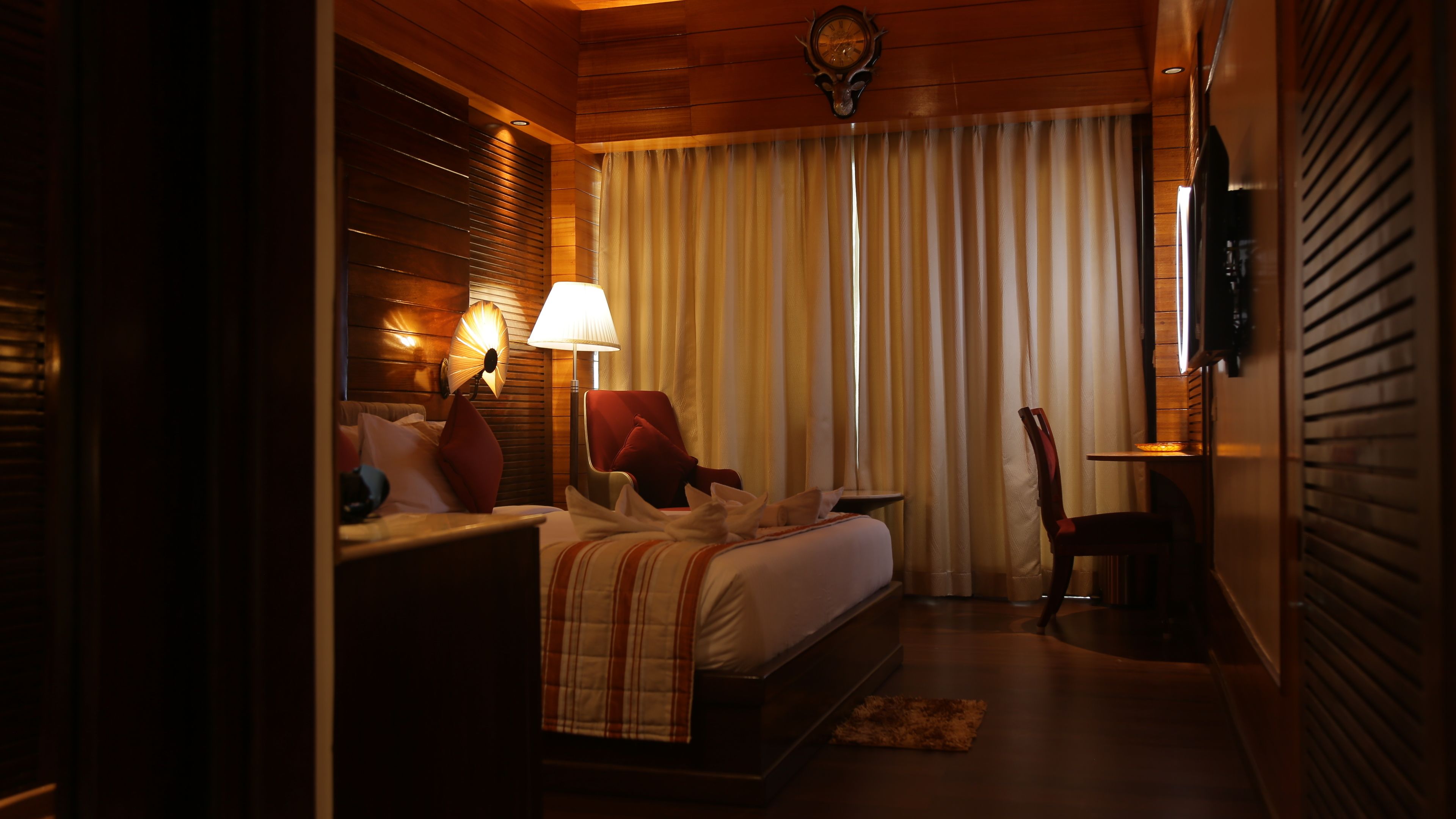 A hotel room with a bed, a nightstand, a lamp, a chair, and a window with curtains.