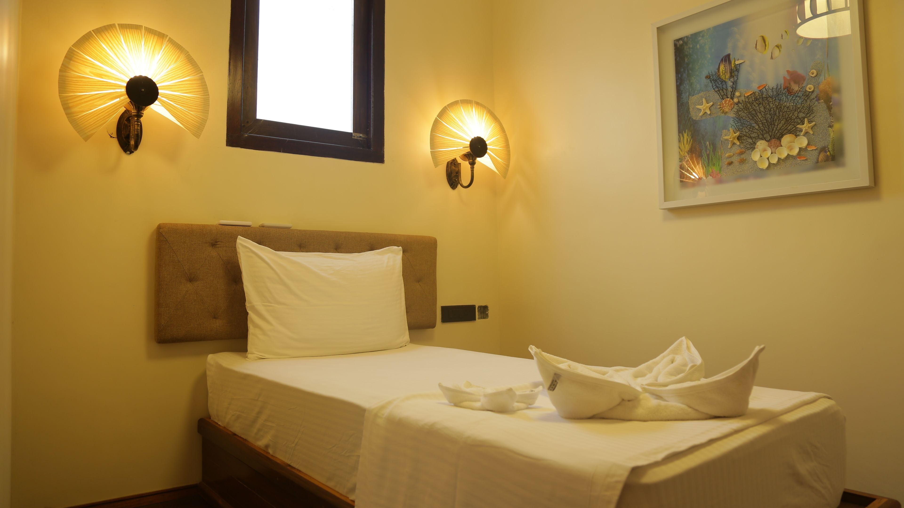 A hotel room with a bed, two wall-mounted lights, a window, and a painting.