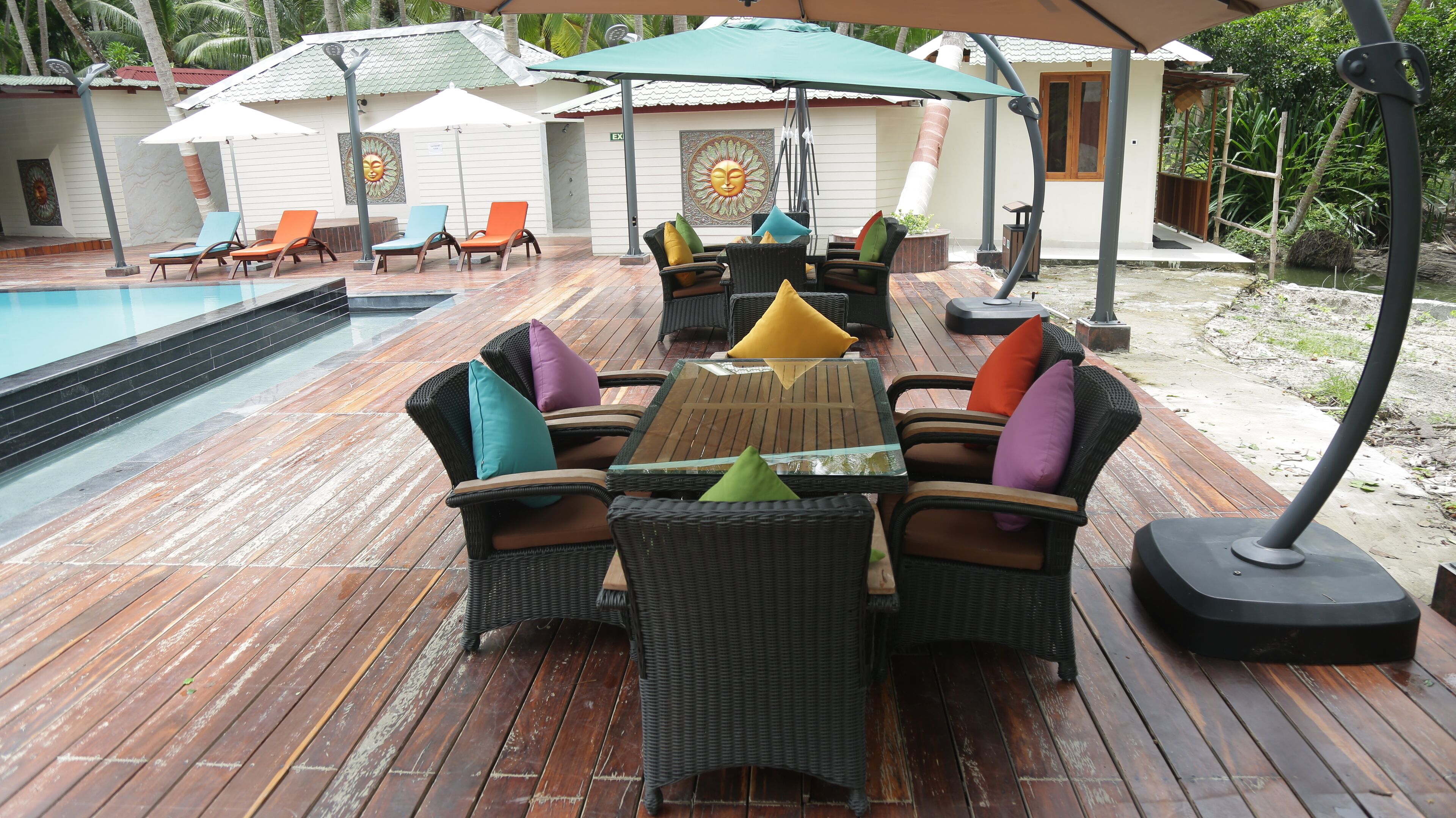 Una terraza de madera con muebles de mimbre, una piscina y sombrillas.