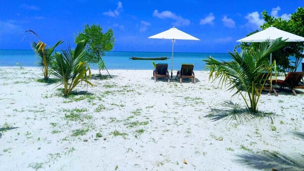 A beach with white sand, two lounge chairs, and a boat in the water. - Sandyy Wavess Beach Resort (Port Blair)