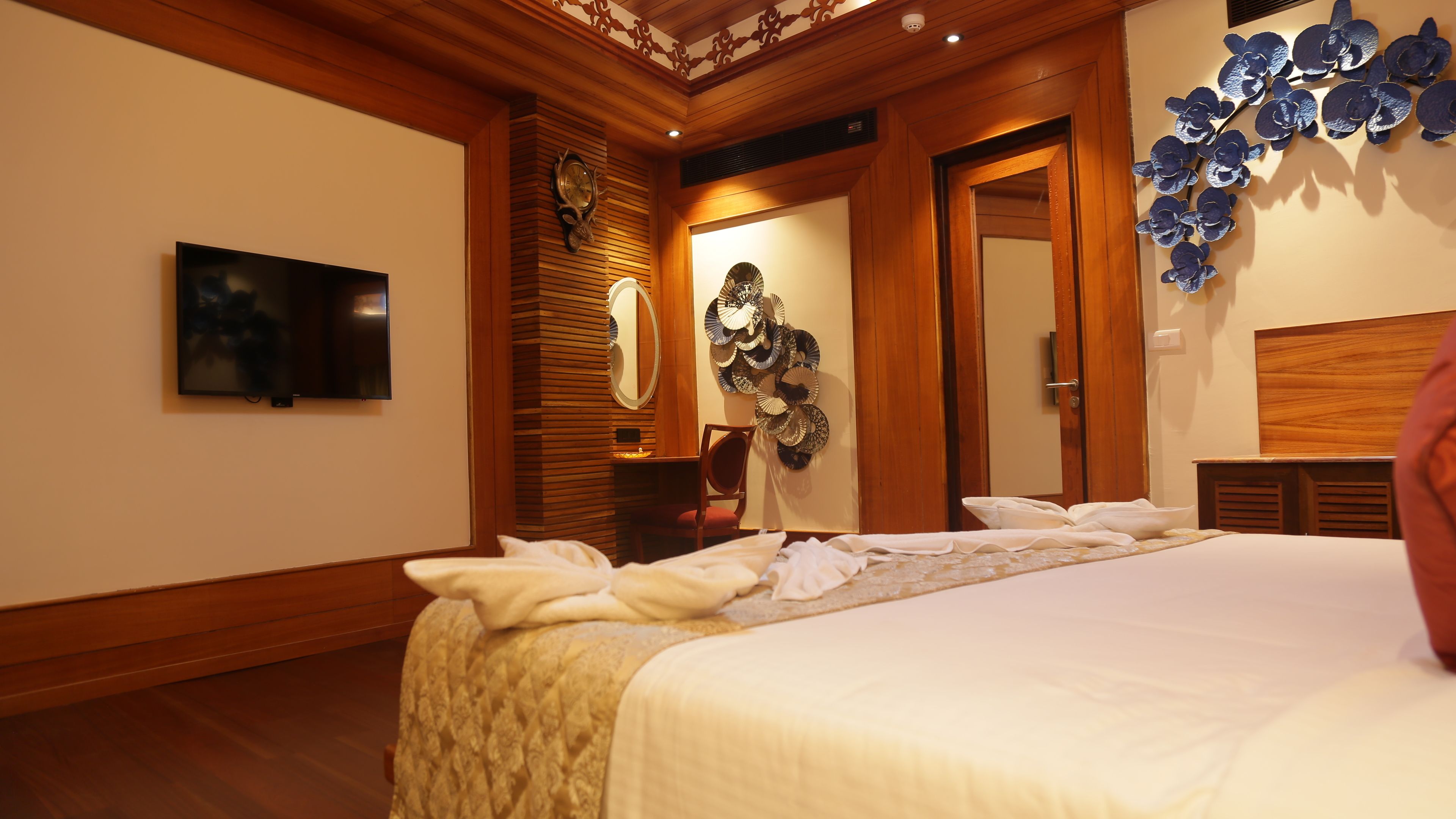 Habitación de hotel con una cama grande, televisión de pantalla plana, techo de madera y un reloj montado en la pared.