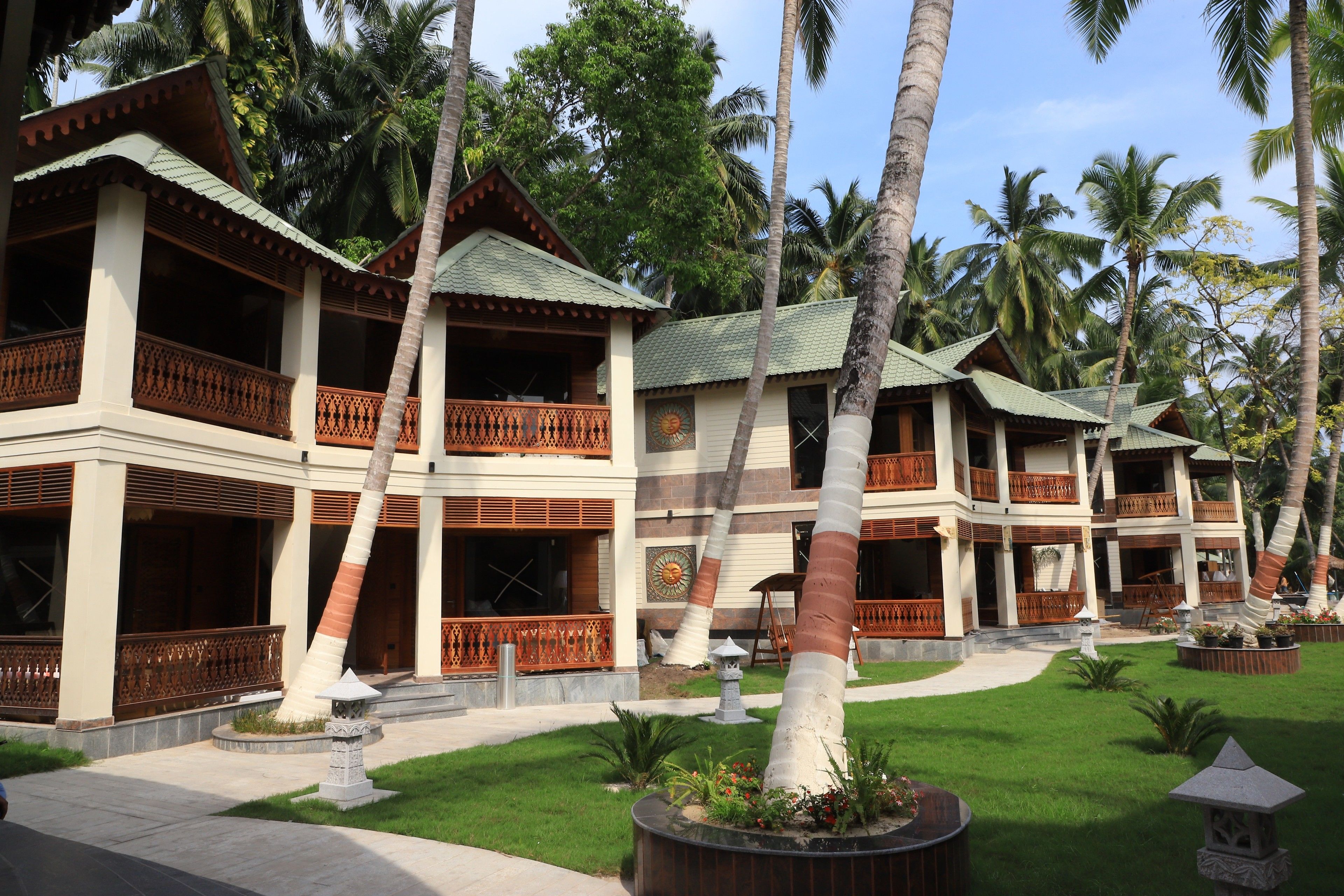 A resort with multiple two-story buildings, each featuring balconies with wooden railings, surrounded by palm trees and well-maintained lawns.